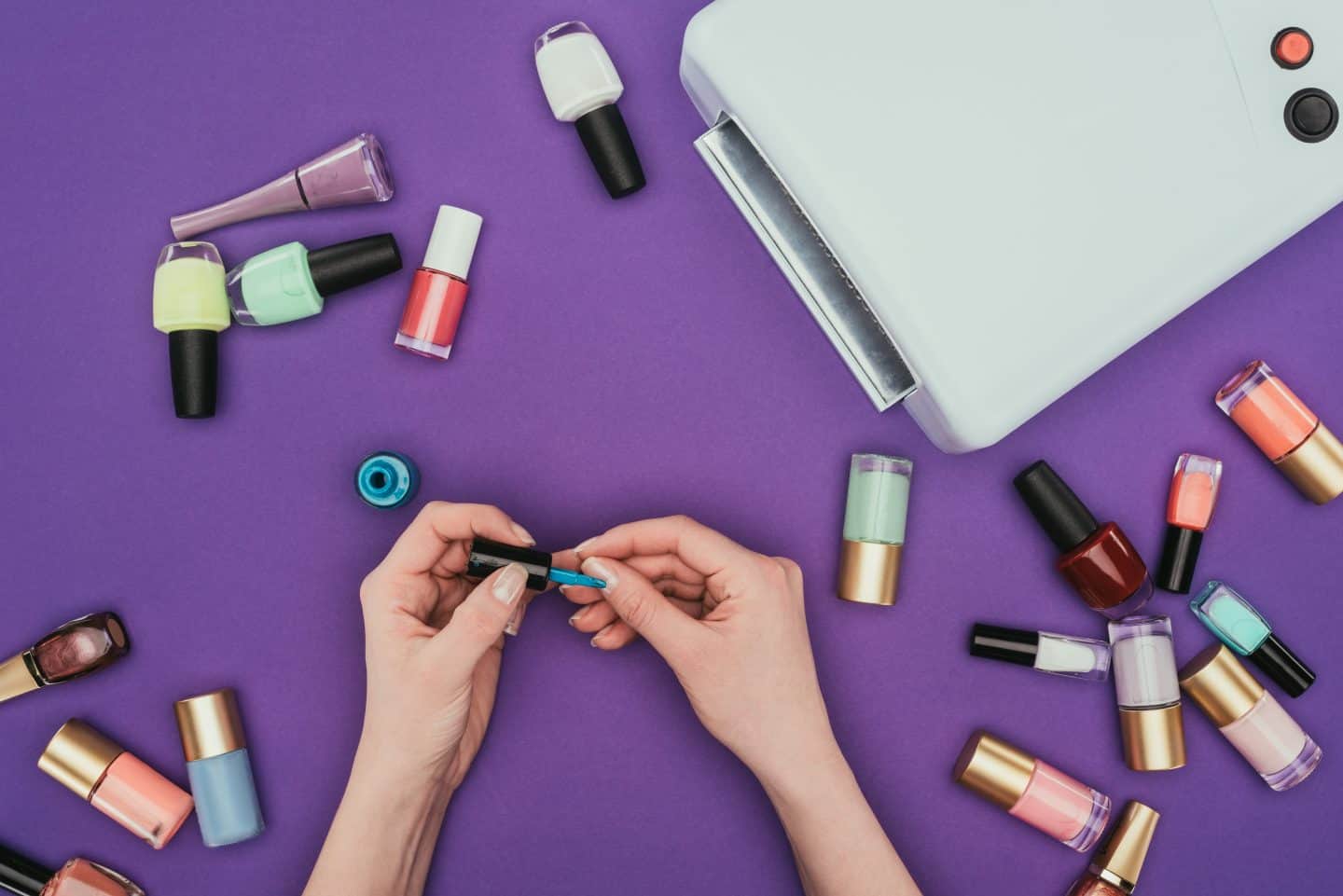 purple background with hands painting nails and lots of nail polish bottles
