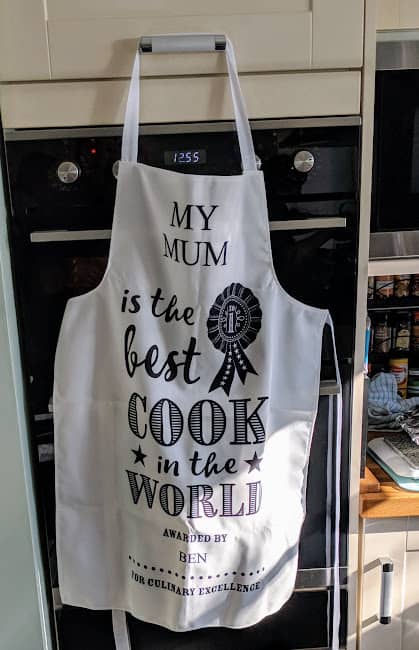 An apron hanging on an oven door with the text "My Mum is the best cook in the world, awarded by Ben for culinary excellence.