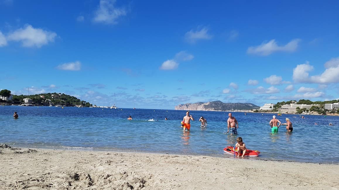 landscape picture of the beach and sea in bright sunshine with people swimming and paddling