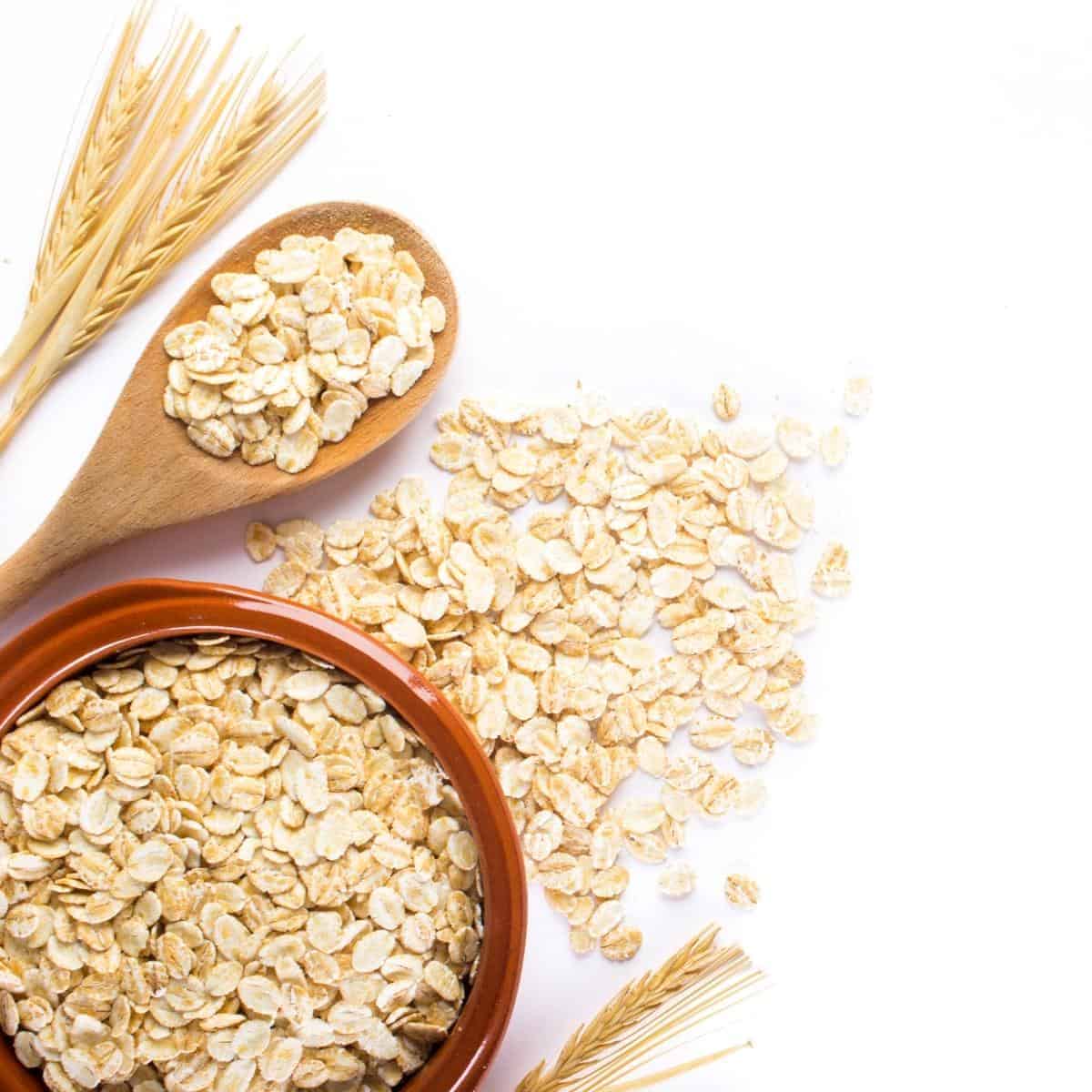 oats in a bowl and on a wooden spoon then spilled onto a white table.