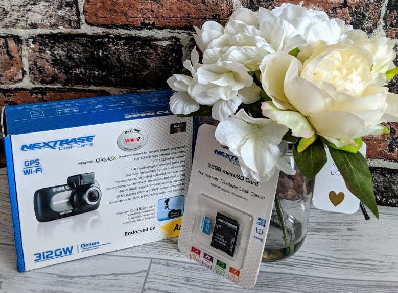 A Nextbase dash cam package is displayed next to a vase of white flowers and a 32GB microSD card, great for ideas as gifts for a car lover