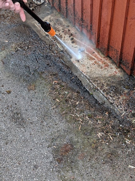 Using the pressure washer to clean concrete areas near a fence