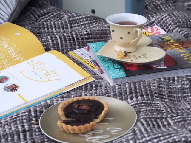 Creativity books with a cup of tea and a chocolate tart on a bed.