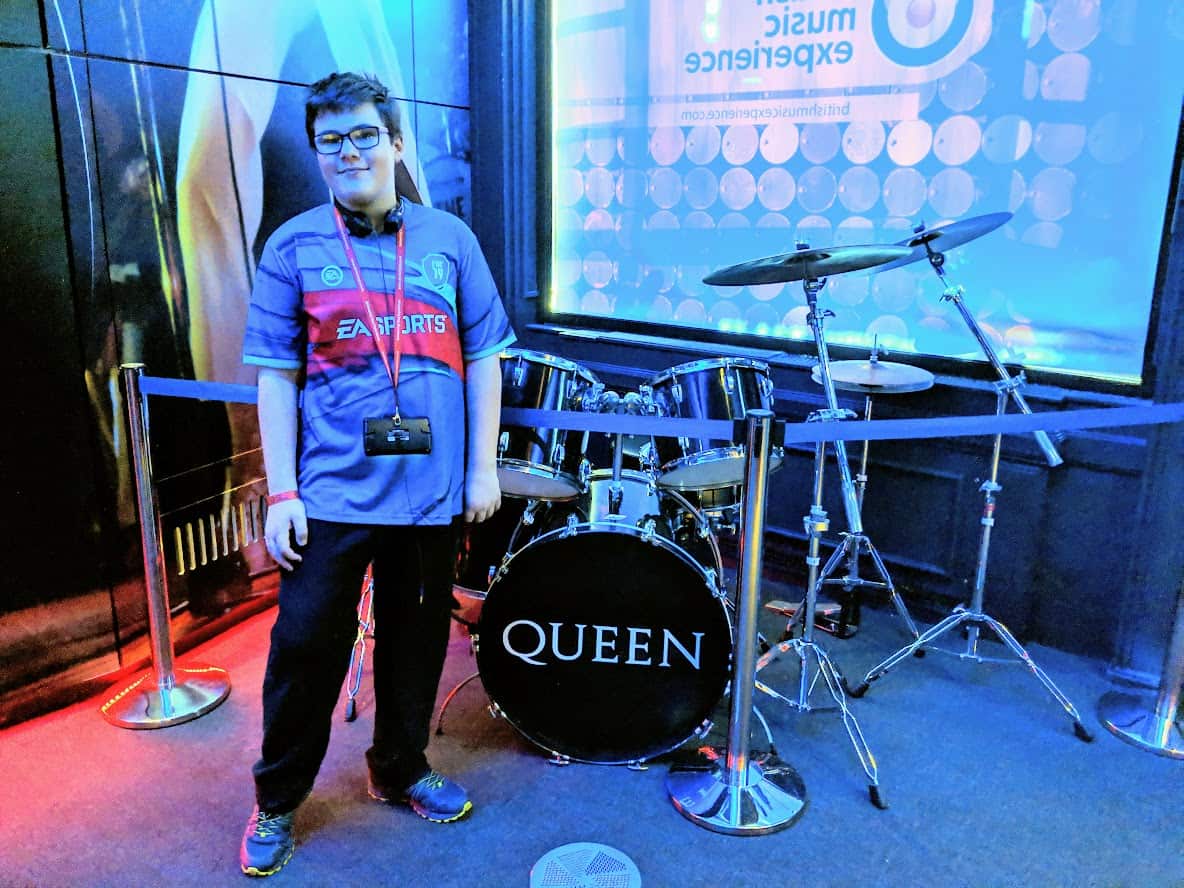 A teenage boy standing in front of a Queen drum set