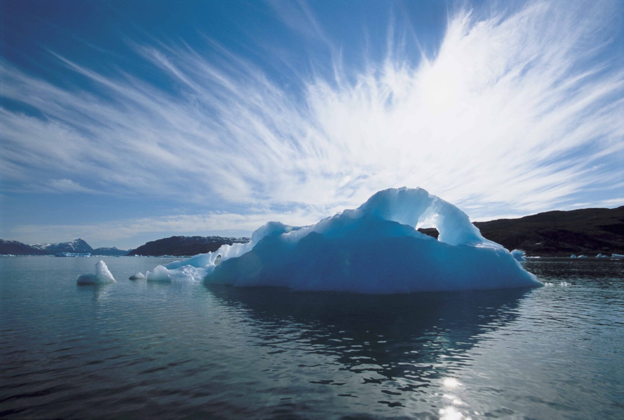 A large iceberg floats in calm water under a sky with streaked clouds, reminiscent of the serene landscapes of Lapland.