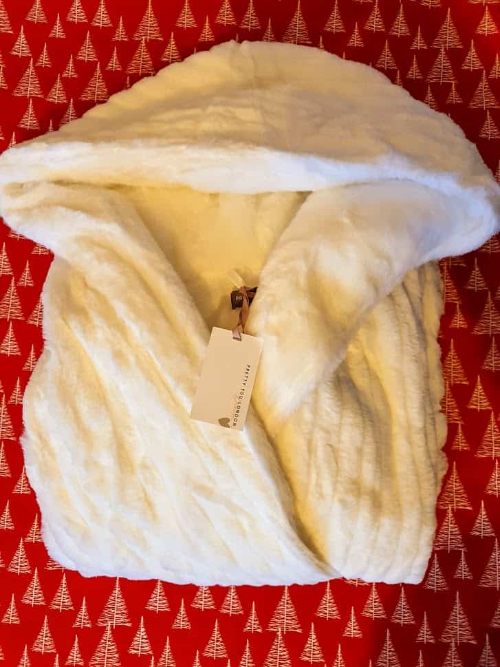 A white, plush robe with a tag is folded neatly on a red background featuring white tree patterns, making it an ideal Christmas gift for her.