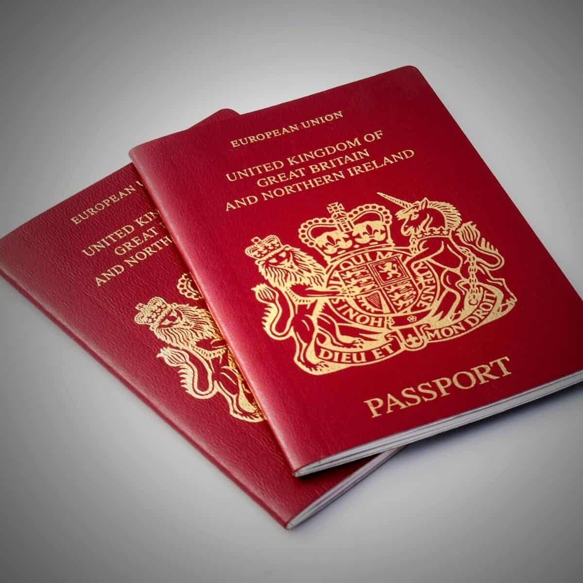 Two burgundy UK passports on a white surface.