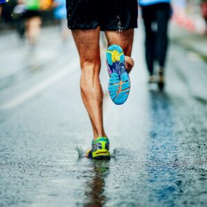 Close-up of a runner’s legs and trainers as they run on a wet, rainy road, splashing water with each step.