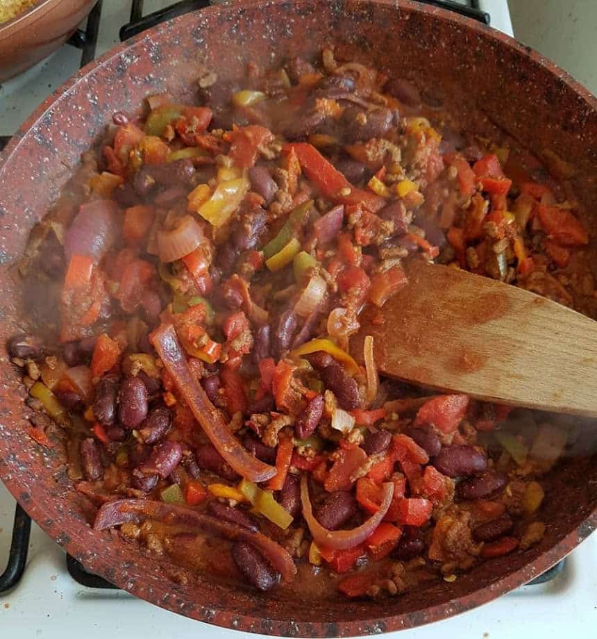 Frying pan of mince chilli with kidney beans, red onions and peppers.