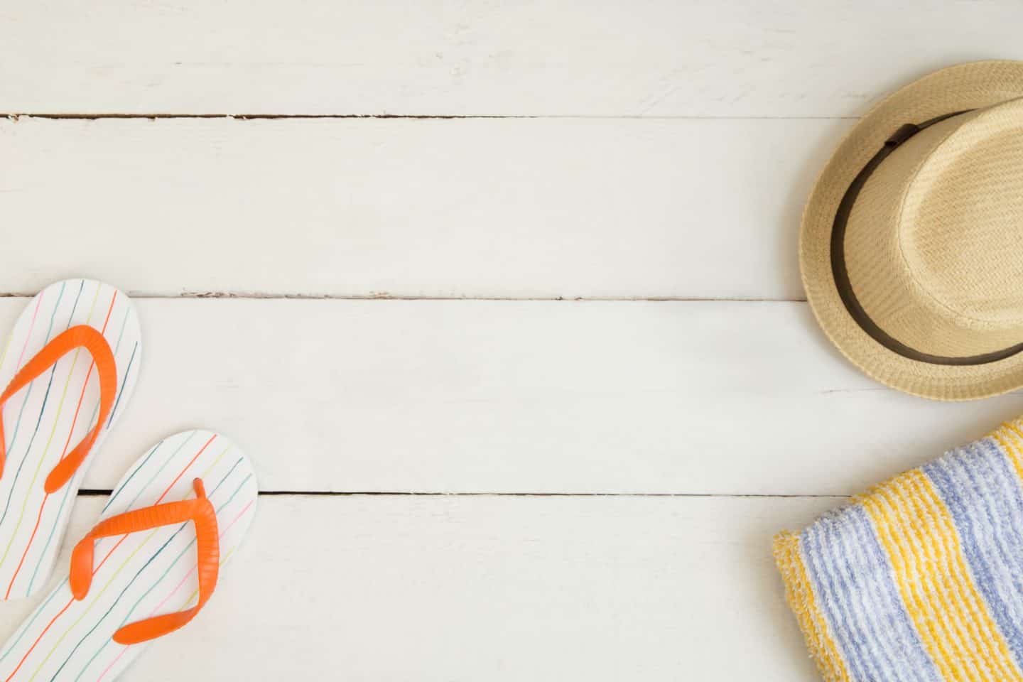 beach hat, flip flops and towel on white wooden deck