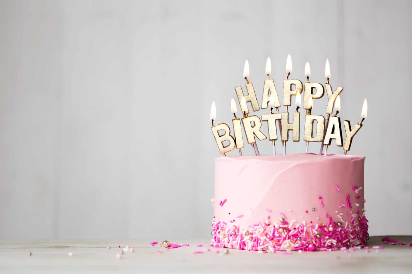 A pink cake with happy birthday candles in front of marble background