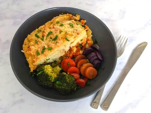Gardeners pie with vegetables on plate with cutlery on right hand side