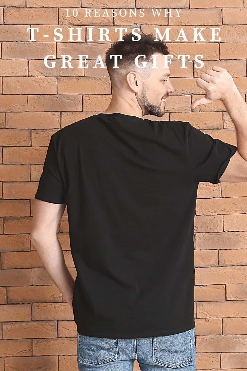 A man standing with back to camera wearing a white shirt in front of a brick wall pointing a thumb to his shirt