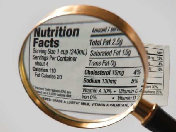 Magnifying glass over nutrition facts section of a food label, the values are irrelevant as the image is just to show labeling