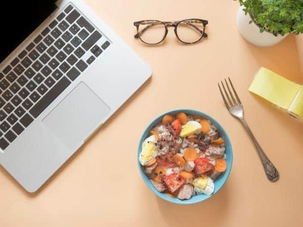 bowl of a rice salad lunch with laptop and glasses on a table