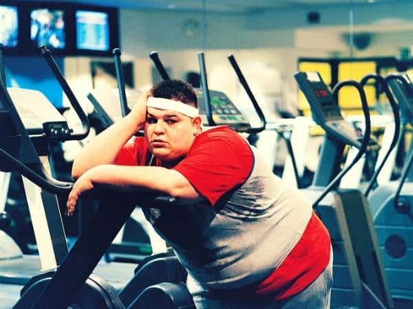 Man leaning unhappily against ab treadmill as he is overweight