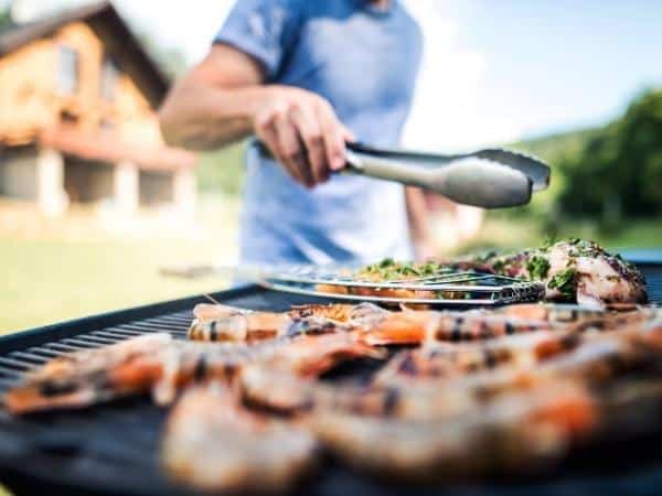 bbq with various meats and a man turning them with silicone tongs.