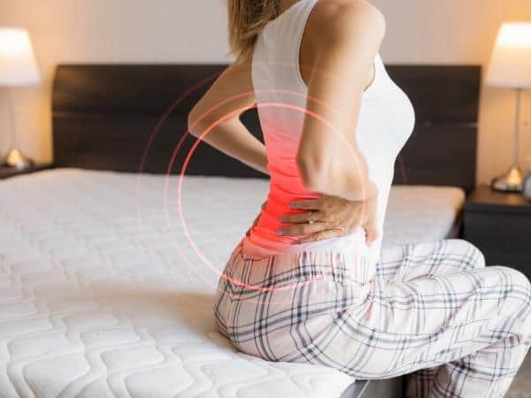 Woman sitting on a bed with fibromyalgia pain in her back and hips