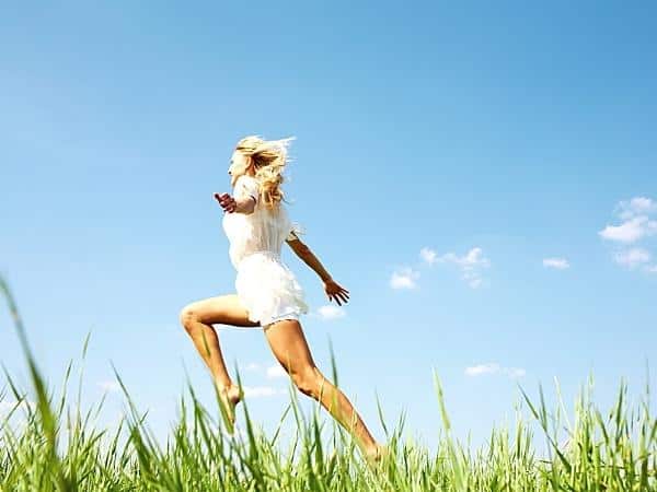 energetic lady running through a field with blue sky