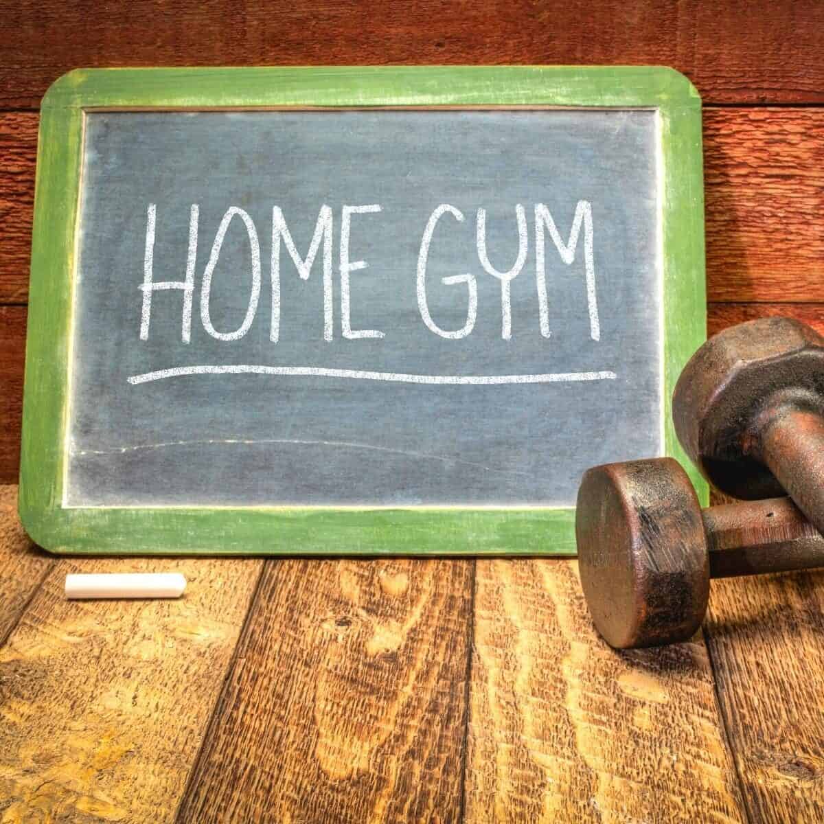 home gym written in chalk on a blackboard with dumbbells in front on wooden floor