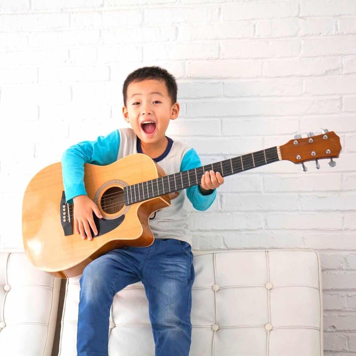 young boy playing a large guitar