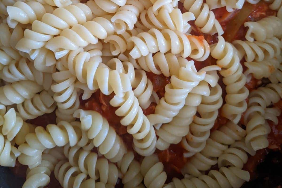 cooked pasta on top of the tomato and mince mix in a frying pan