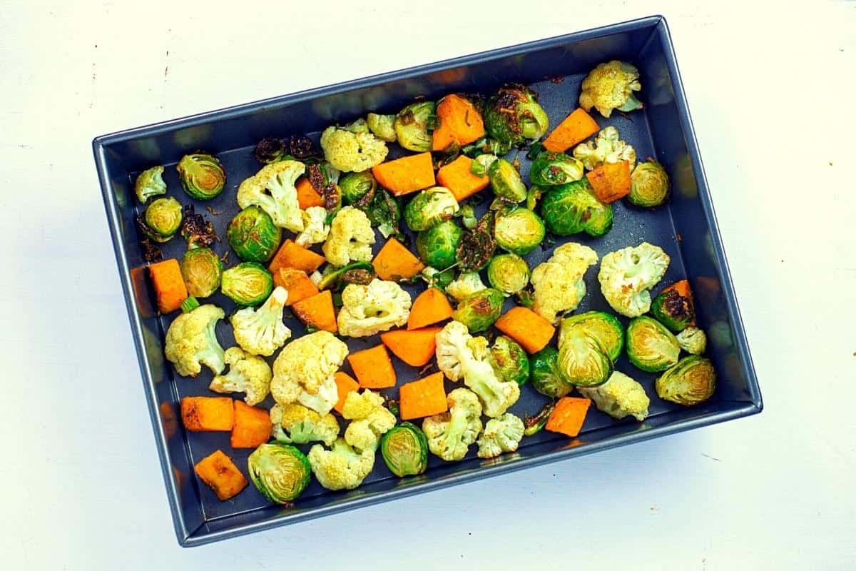 A delicious roasted vegetable salad featuring cauliflower, Brussels sprouts, and sweet potato chunks arranged in a rectangular baking pan.