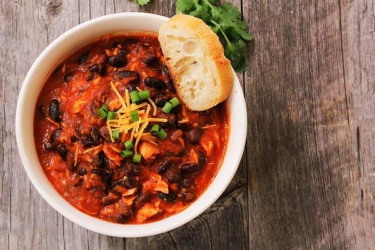 turkey mince chilli in a white bowl with garlic bread on the side