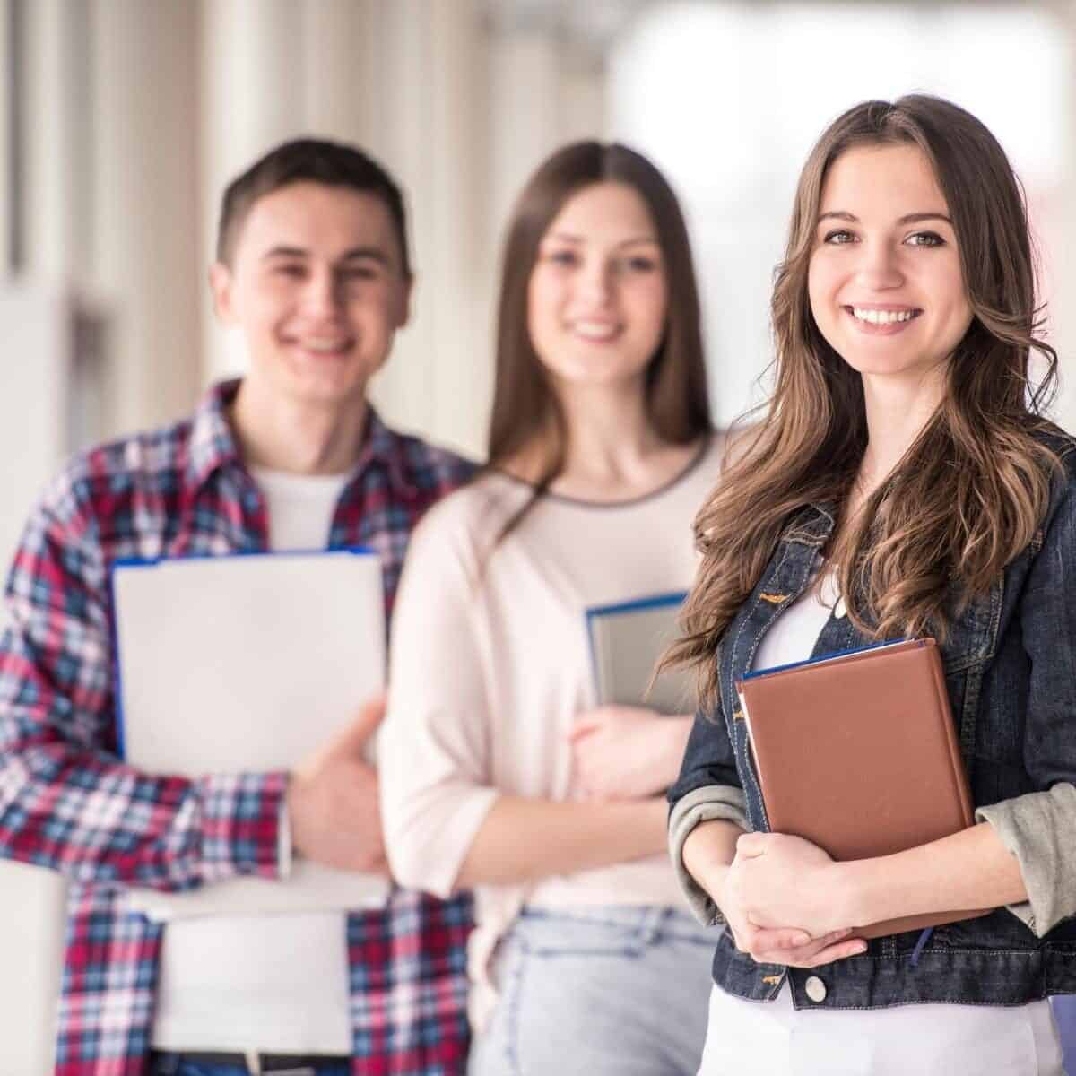 three students standing smiling holding books