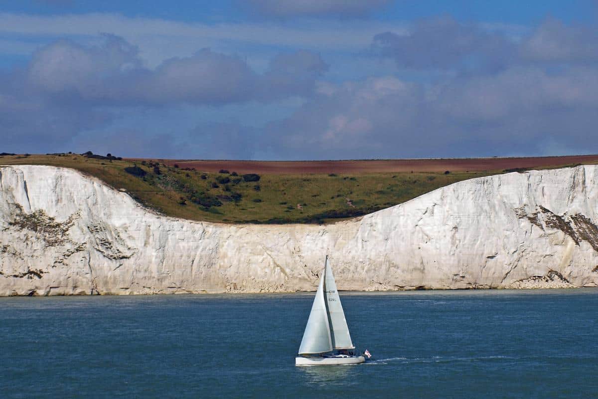 A sailing boat on water in front of the white cliffs of Dover.
