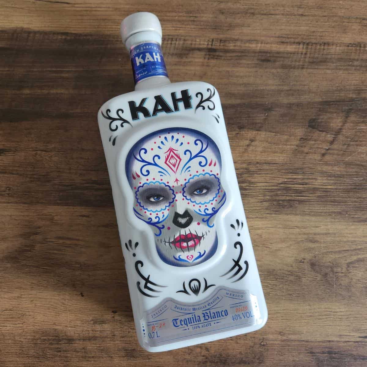 Bottle of KAH tequila which is a white bottle with a decorated skull in a day of the dead type theme.