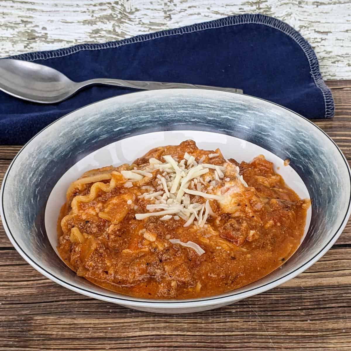 bowl of lasagne soup on a wooden table with a blue napkin and spoon