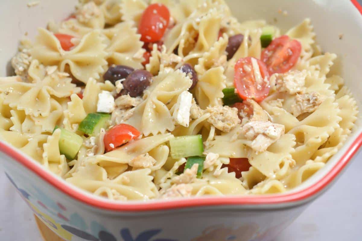 A delightful bowl of Greek pasta salad featuring farfalle, cherry tomatoes, olives, cucumber, succulent chicken, and tangy feta cheese.