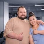 Couple of overweight people with their thumbs up in a gym.