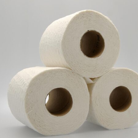 Three rolls of white toilet paper are stacked in a pyramid shape against a plain, light grey background.