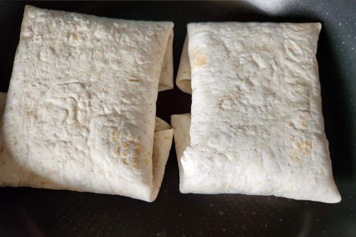 Two folded and uncooked burritos in a frying pan.