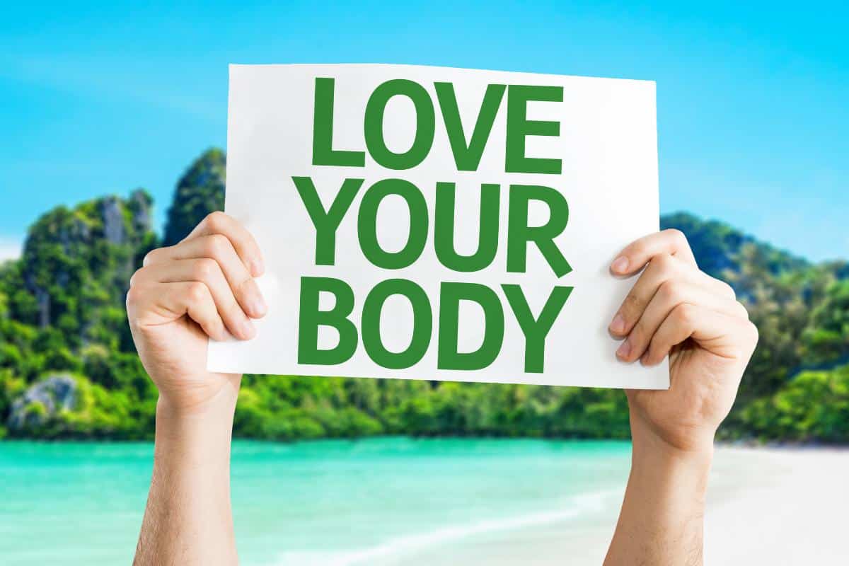 Hands holding up a printed sign saying love your body.