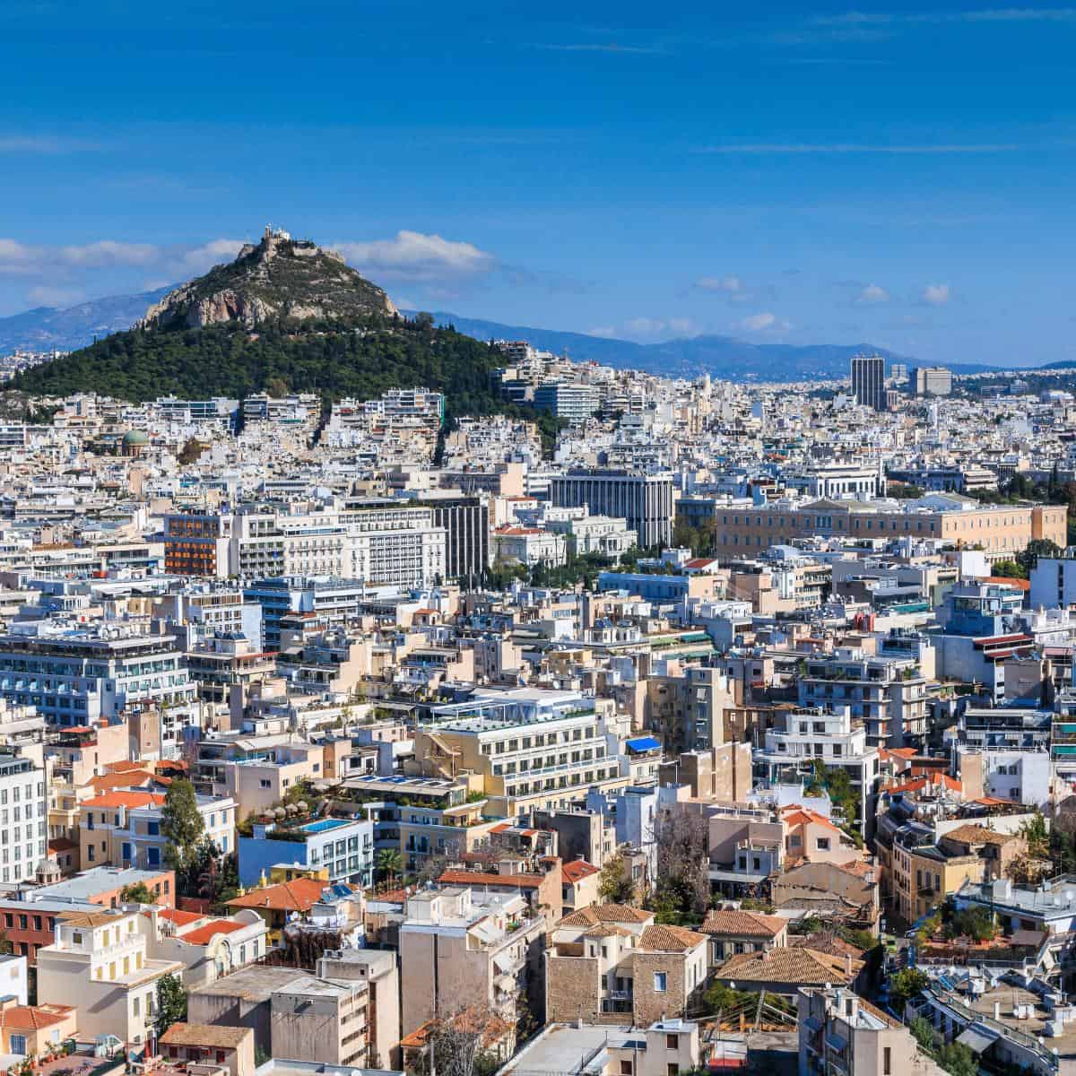 Aerial view of Athens for couples, showcasing dense urban buildings with Mount Lycabettus in the background under a clear blue sky.