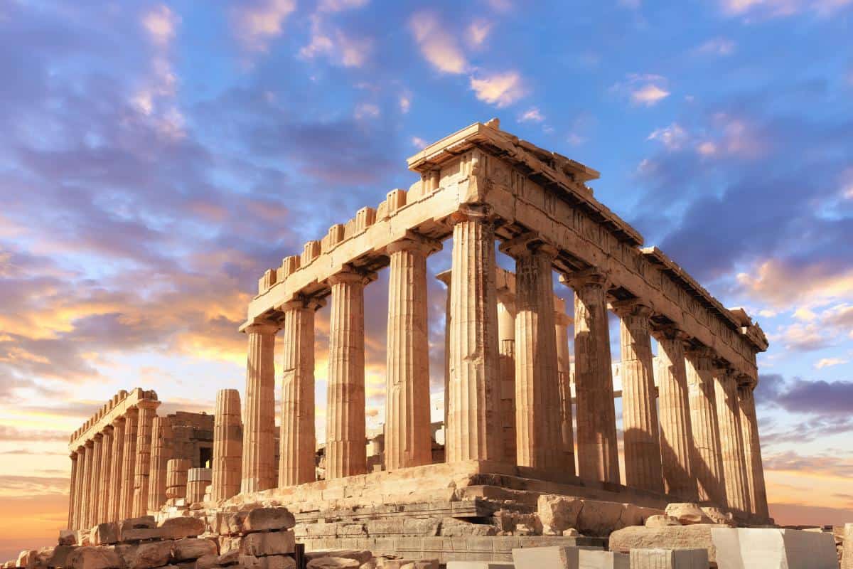 The Parthenon in Athens, Greece, offers couples a romantic view with its tall columns and partially complete structure set against a vibrant sky filled with clouds and the enchanting hues of sunset.