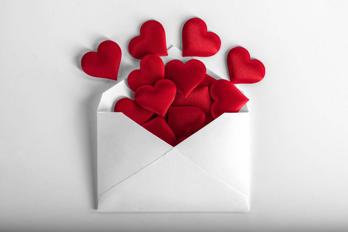 White envelope with red hearts coming out of it.