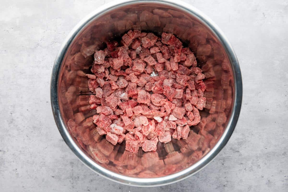 slow cooker bowl with beef chunks coated in corn flour.