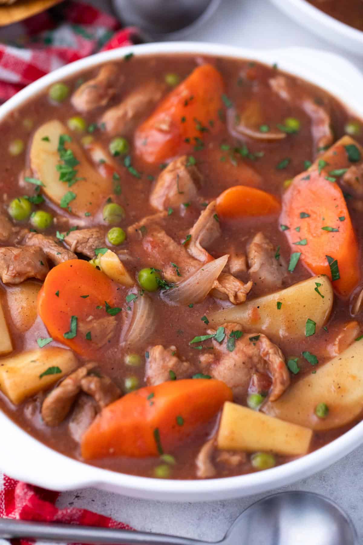 A bowl of hearty guinness lamb stew with tender chunks of beef, carrots, potatoes, peas, and onions in a thick broth, garnished with chopped parsley.