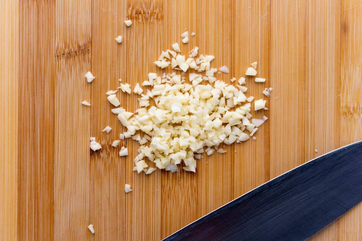 Wooden chopping board with a knife and finely chopped garlic.