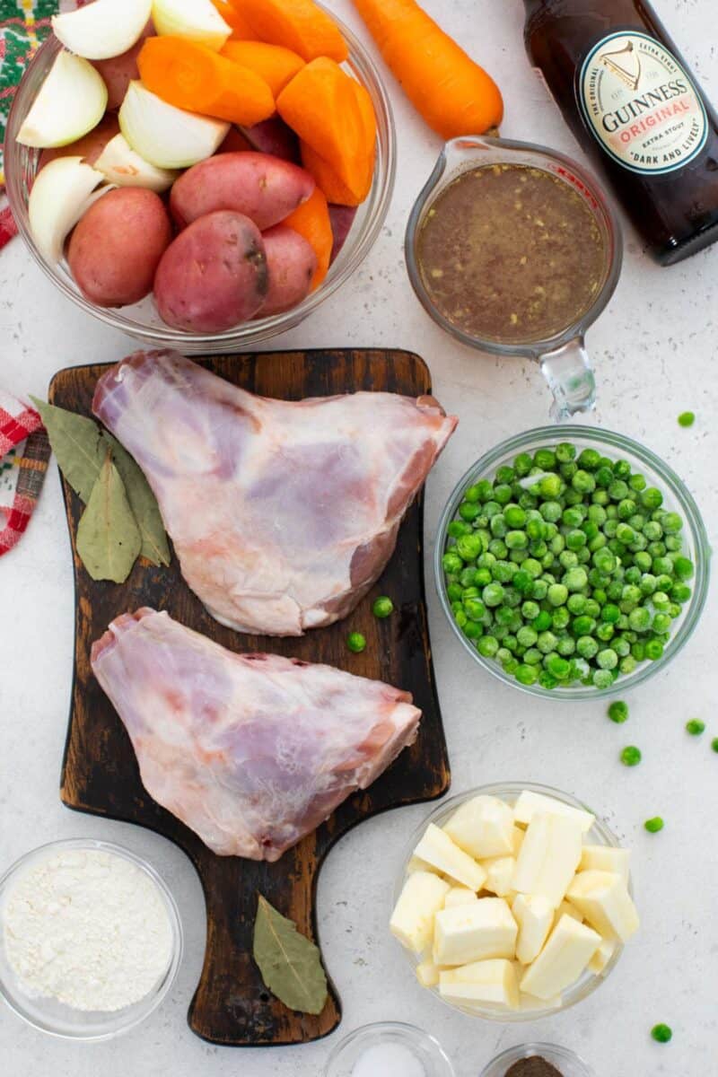 Irish stew ingredients laid out with red potatoes, carrots, frozen peas, stock, Guinness, and lamb.