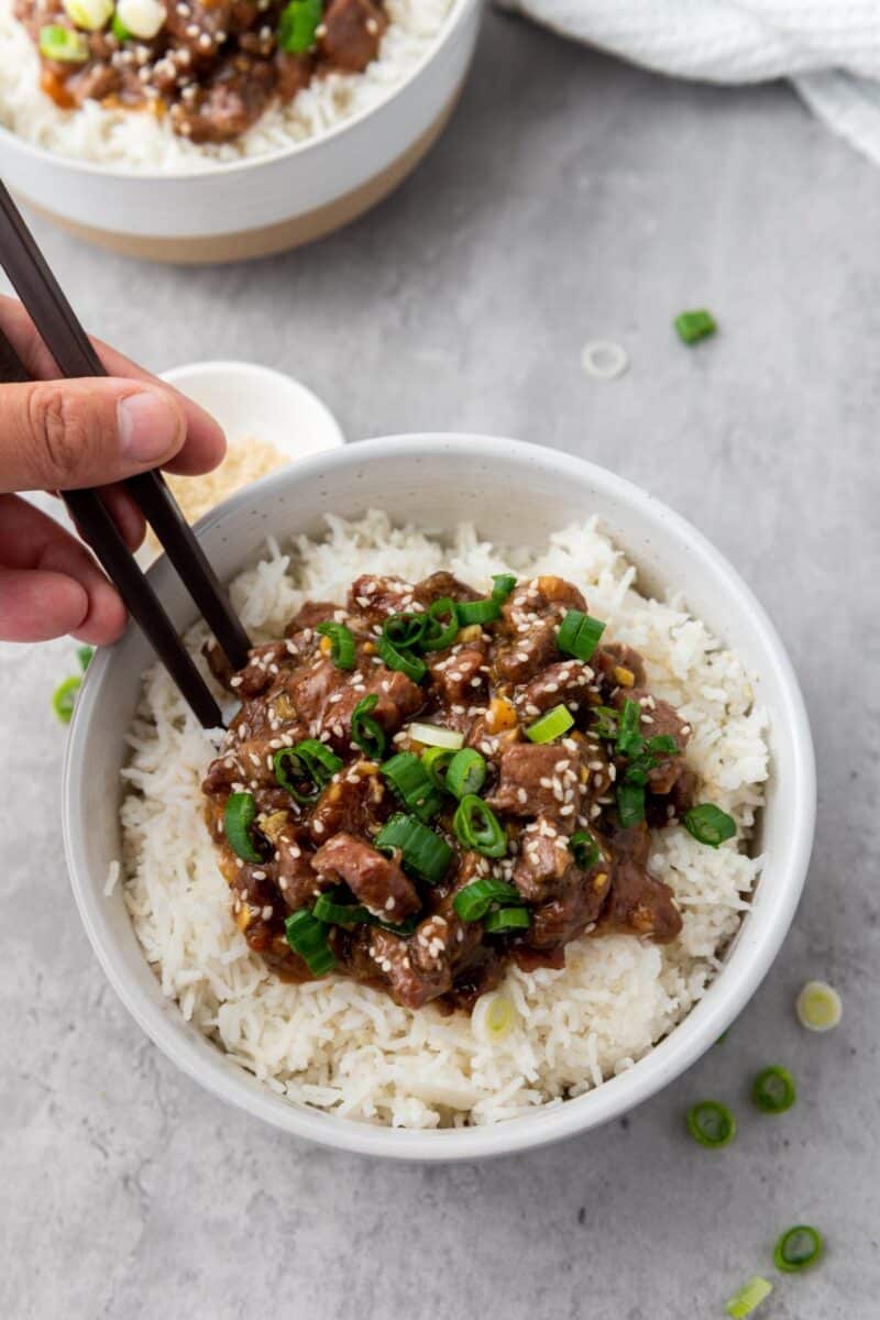 Bowl of Mongolian beef with a hand using chopsticks to pick up a small amount.