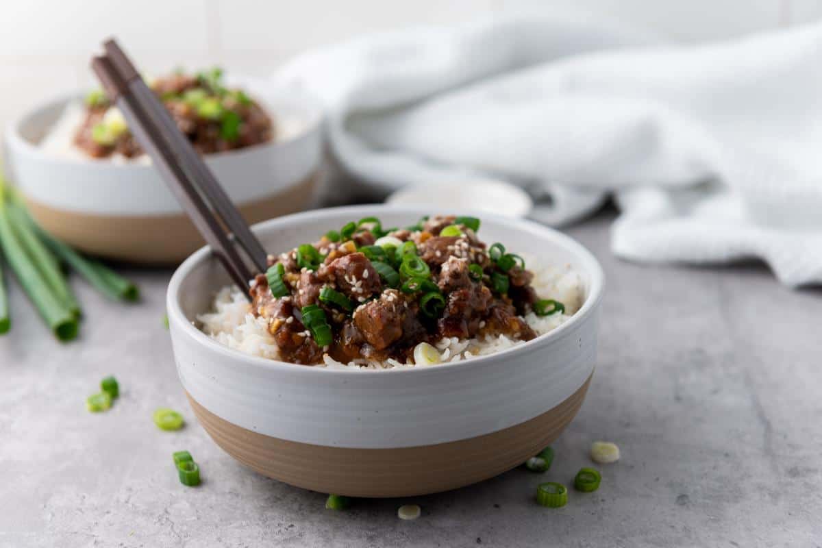 A bowl of rice and Mongolian beef topped with spring onions.