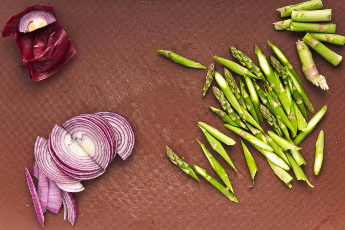 red onion and asparagus chopped on a chopping board.