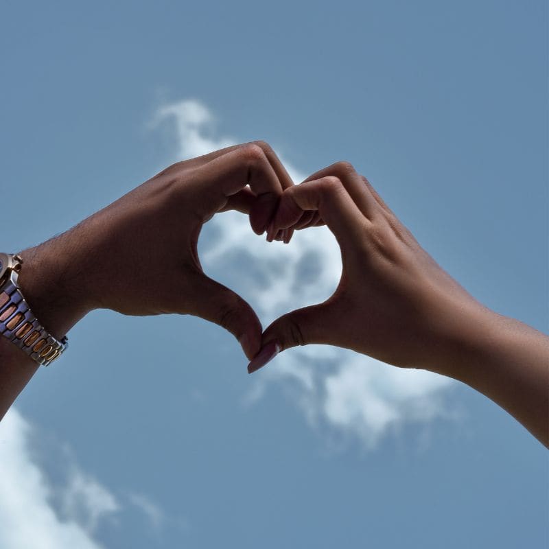 Two hands forming a heart shape against a blue sky with clouds, beautifully illustrating one of the universal love languages.