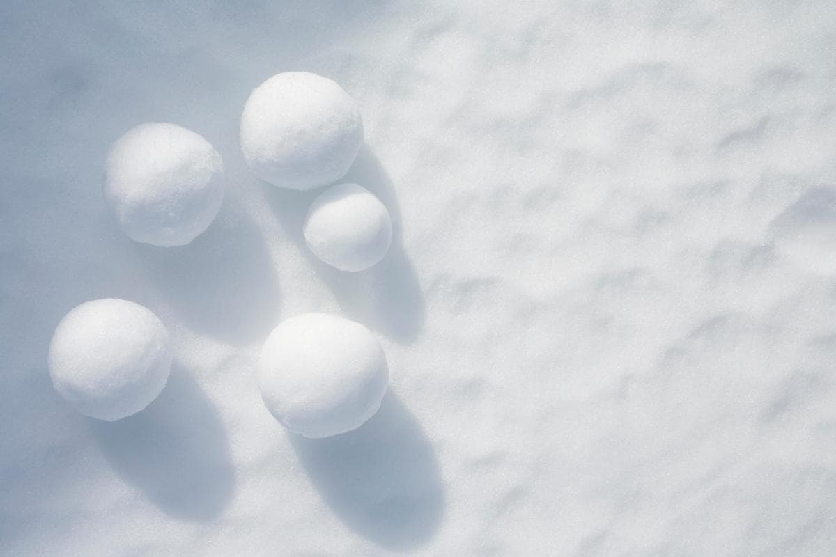 five different sized snowballs freshly rolled on a floor of crisp white snow.