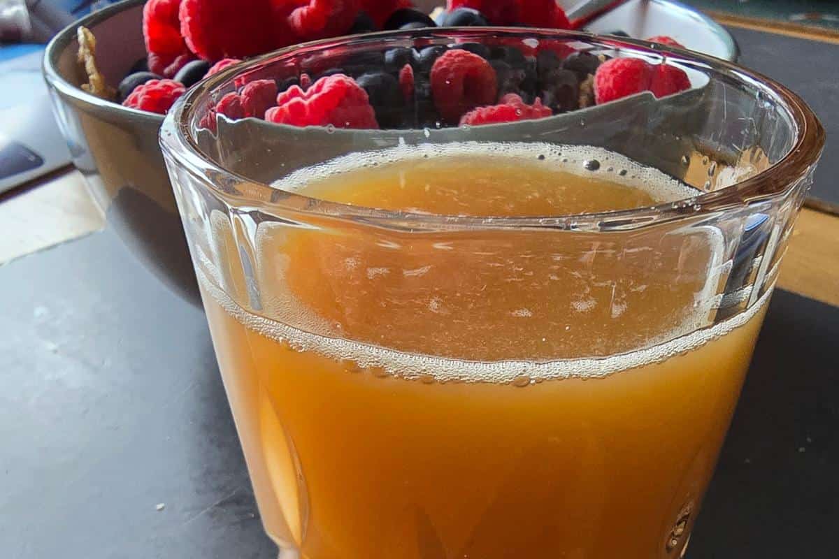 A glass of freshly squeezed orange juice, crafted with a juicer, sits in the foreground, with a bowl of vibrant raspberries and blueberries in the background.